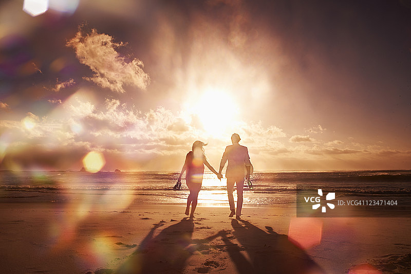 一對情侶在海灘上散步，夕陽下的剪影圖片素材