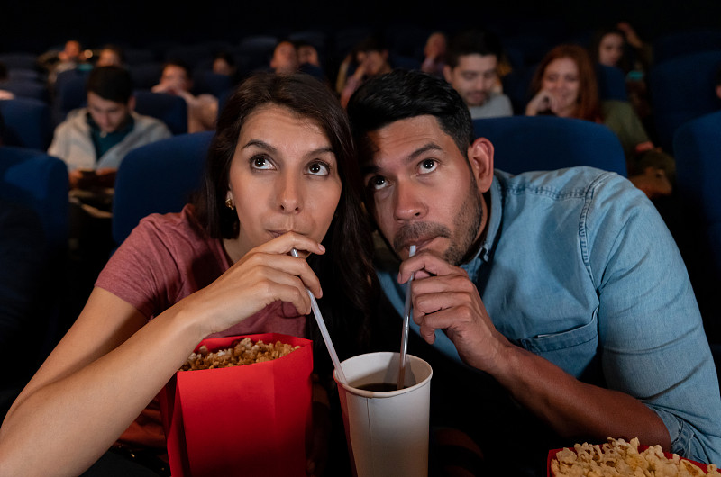 一對幸福的情侶在看電影，一個女人在吃東西，一起喝酒圖片素材