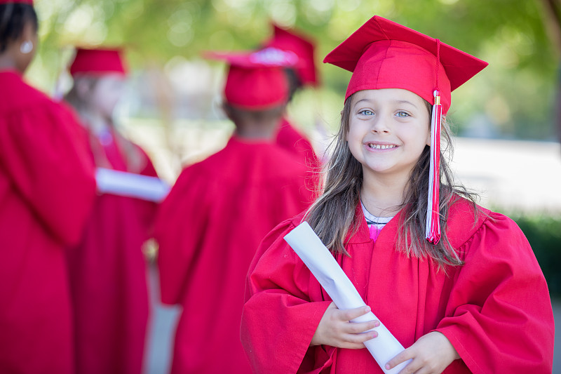 可愛的學齡前小女孩拿著畢業證書，戴著畢業帽，穿著畢業服圖片素材
