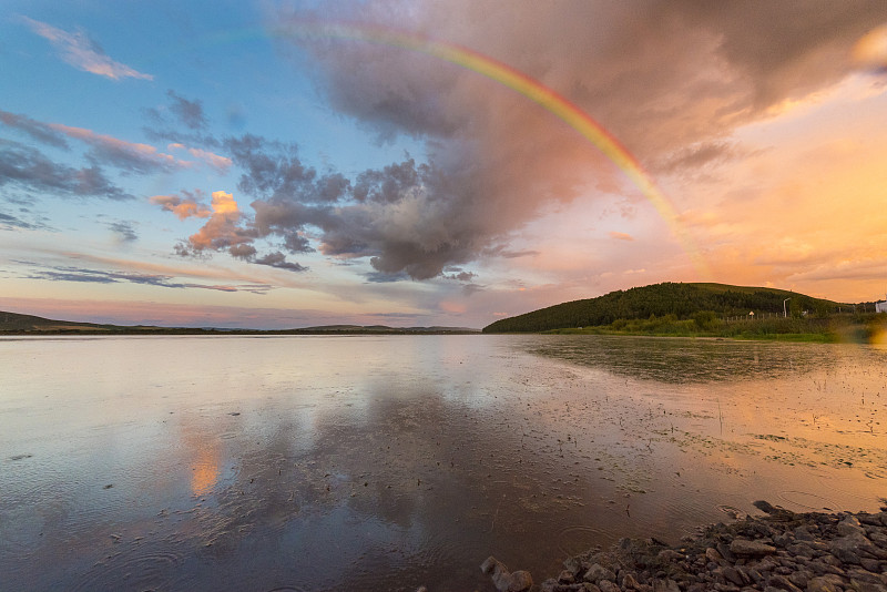 雨后的湖面水平如鏡，倒影出多彩的霞光，一道彩虹掛在天邊圖片素材