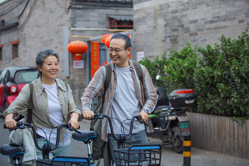 老年人City walk系列:老年夫妇推着共享单车在北京胡同旅行图片下载
