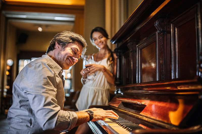 一個英俊的男人在餐館為他的妻子彈鋼琴圖片素材