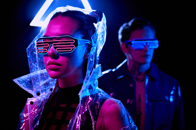 年輕的網絡女人的肖像在未來的眼鏡和透明夾克在前景，男人在霓虹燈眼鏡站在背景圖片素材