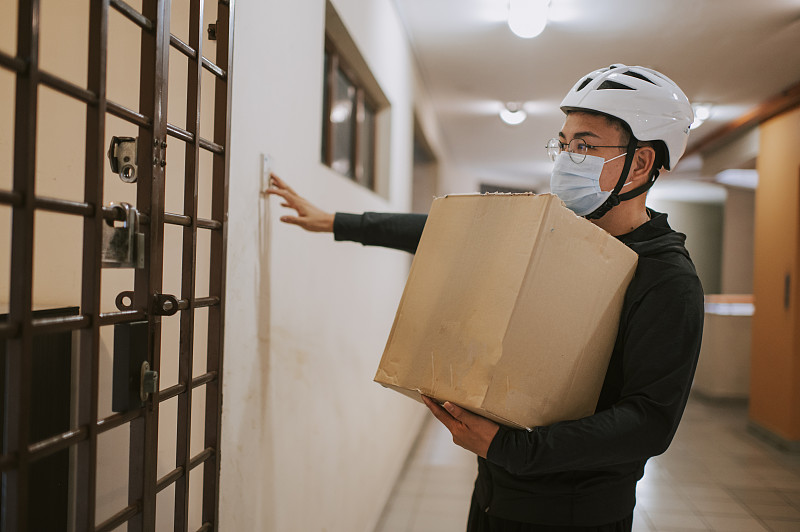 an asian chinese delivery man with helmet and surgical mask press door bell for grocery delivery圖片素材