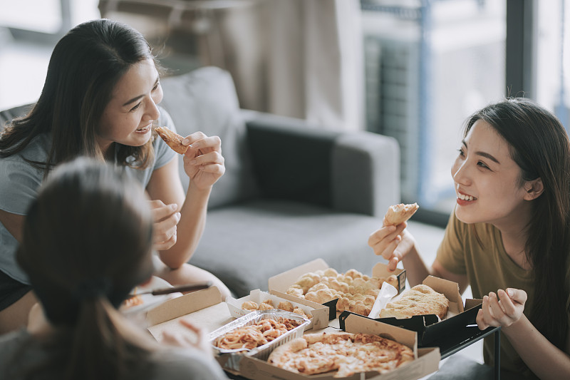 3位亞洲華人女性朋友在客廳吃披薩作為午餐圖片素材