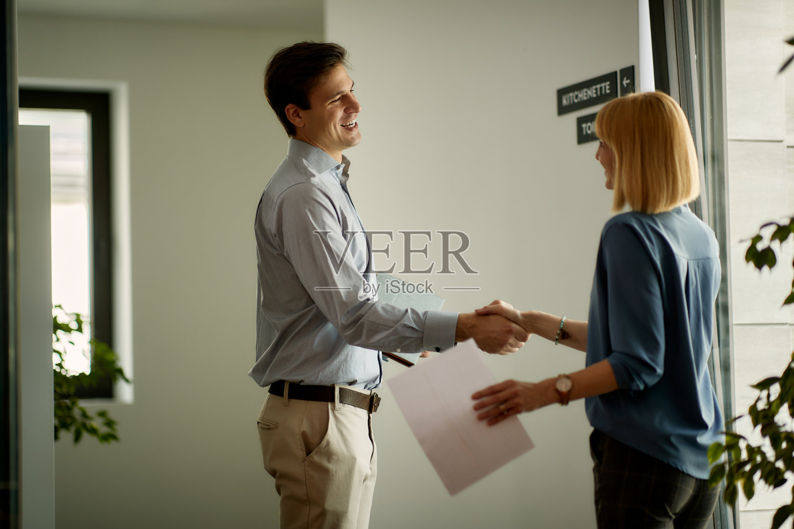 在办公楼的走廊里，快乐的商人与女同事握手。照片摄影图片