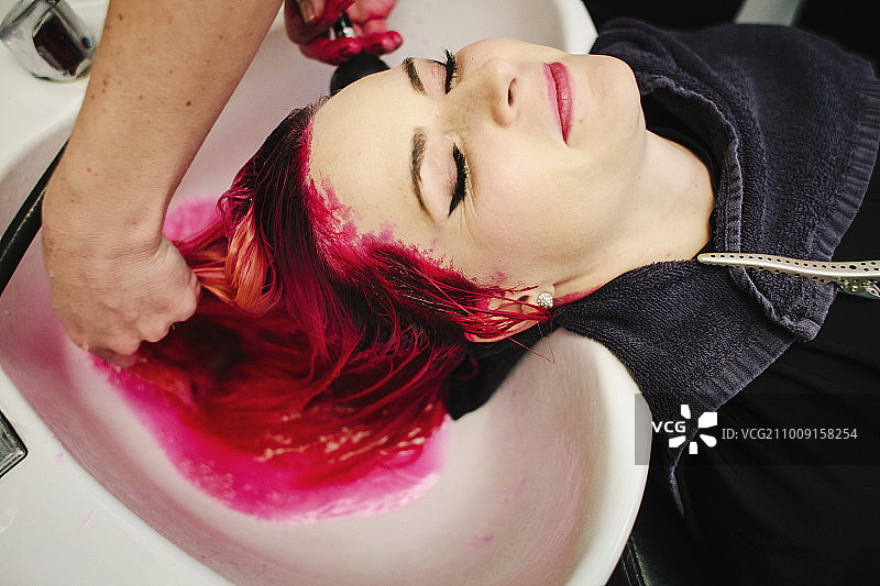 一位发廊的顾客正在用盆子冲洗染红的头发。图片素材