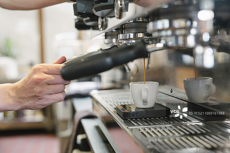 一个男人站在一个浓缩咖啡机前的特写，新鲜的浓缩咖啡跑进一个杯子。图片素材