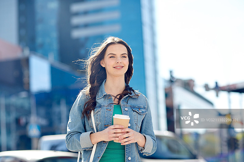 饮料和人们的概念-快乐的年轻女子或少女喝咖啡从纸杯在城市的街道。快乐的年轻女子在城市街道上喝着咖啡图片素材