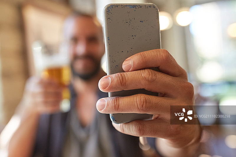 人，休闲和技术概念-近距离的男人与智能手机喝啤酒和在酒吧或酒吧自拍图片素材