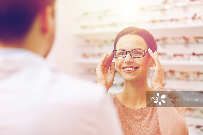 健康，人，视力和视觉概念-幸福的女人选择和展示眼镜在光学商店图片素材