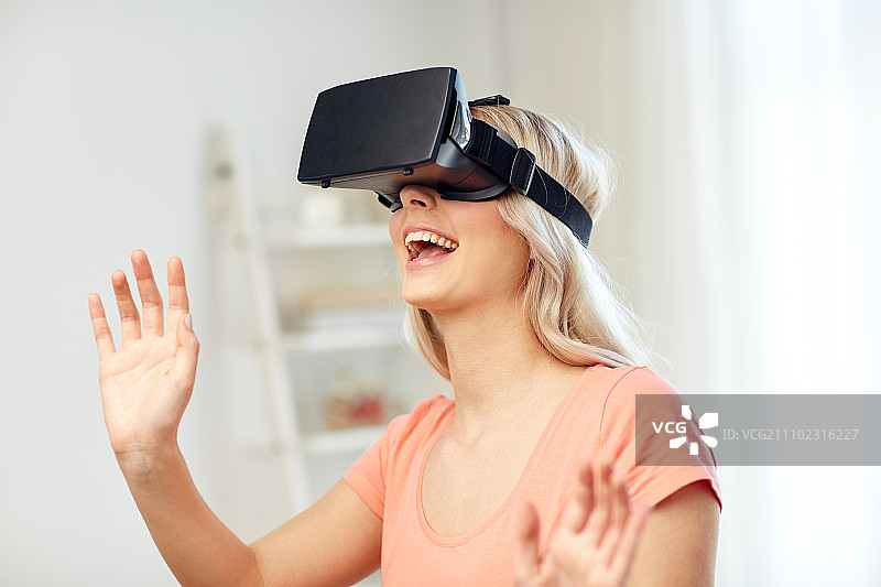 技术，虚拟现实，娱乐和人的概念-快乐的年轻女性用虚拟现实头戴式耳机或3d眼镜在家里玩游戏和触摸看不见的东西图片素材