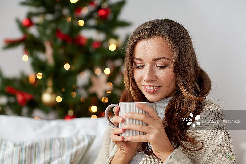 圣诞节、节假日和人们的概念——快乐的年轻女子在家里喝杯咖啡或茶图片素材