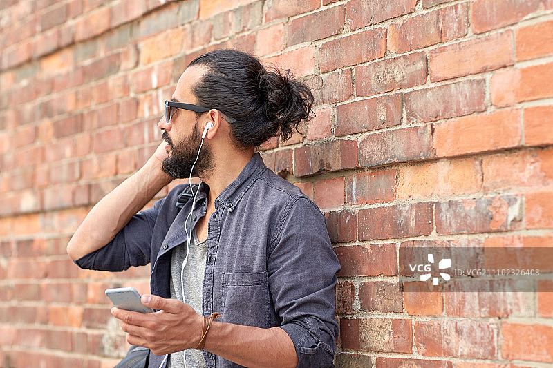 人与技术概念-近距离的人与耳机和智能手机听音乐在砖墙上的街道。街上戴着耳机和智能手机的男人图片素材