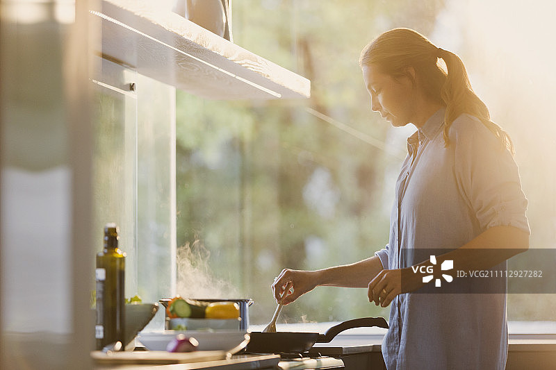 在阳光明媚的厨房里，一个女人在炉子前做饭图片素材