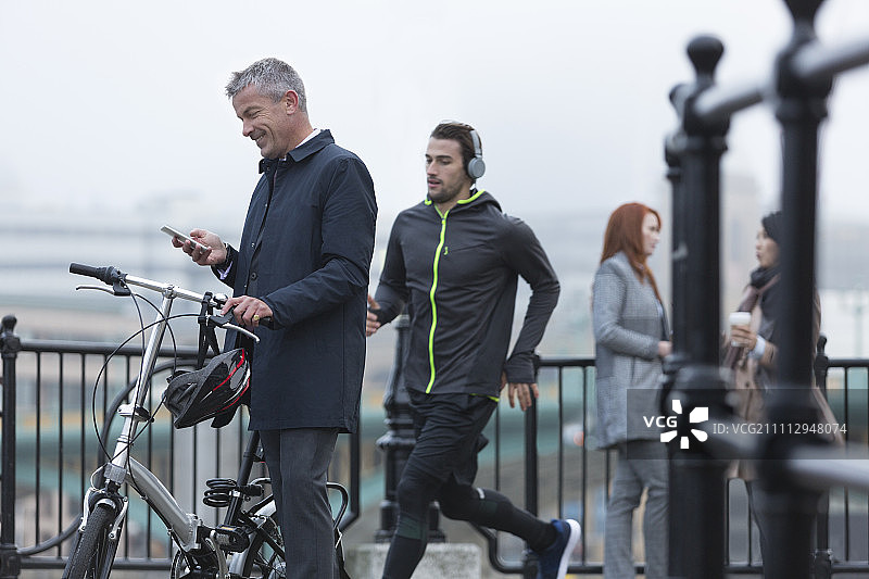 商人与自行车短信与手机和男性跑步在城市匝道图片素材