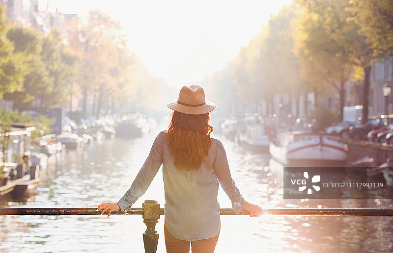 戴着帽子的女人看着阳光明媚的秋天运河的景色，阿姆斯特丹图片素材