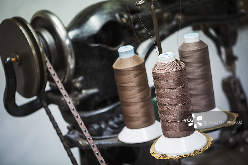 在鞋匠的车间里，一个有强力线或线的线轴的独立皮革缝纫机的特写。图片素材