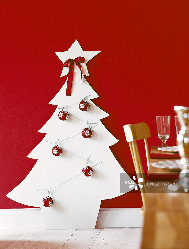 用胶合板做成的白色圣诞树，上面装饰着红色的小装饰品和丝带图片素材