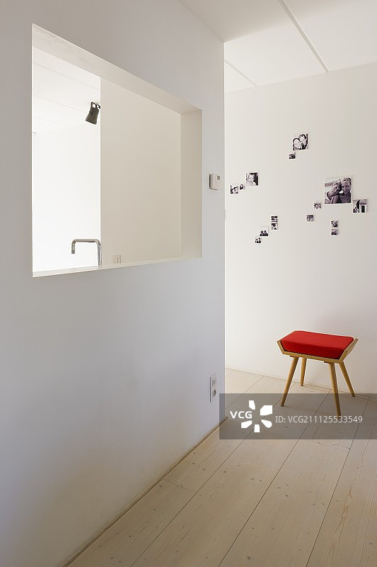 带有红色衬垫的凳子位于一个简单的、极简主义的大厅里，穿过一堵可以看到厨房水龙头的墙图片素材