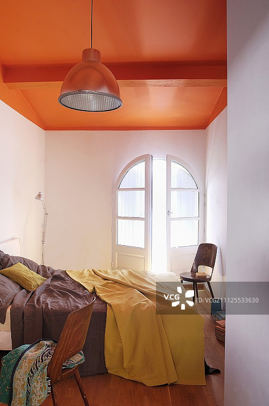 狭窄的卧室采用了简单的工业风格，天花板漆成大胆的橙色图片素材