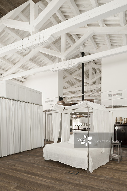 阁楼公寓的白色屋梁下的睡觉区，配有白色织物顶棚的四柱床图片素材