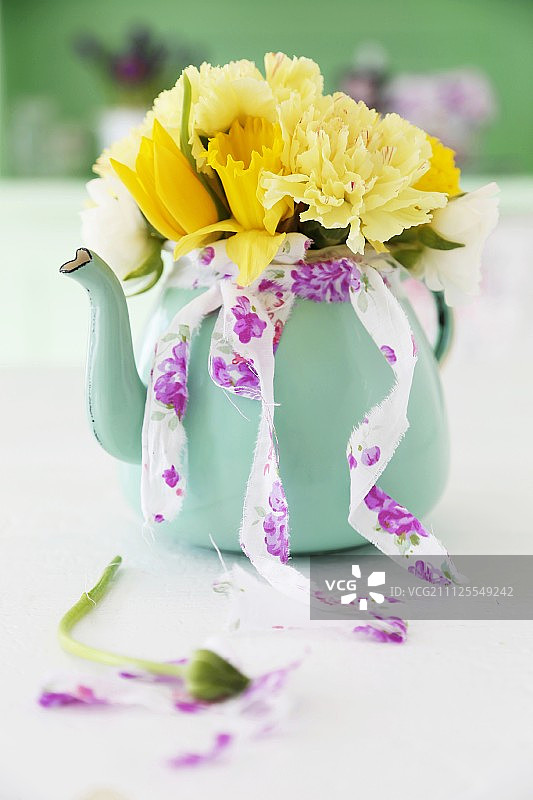 黄色的春天花朵郁金香，康乃馨和水仙花在绿松石茶壶图片素材