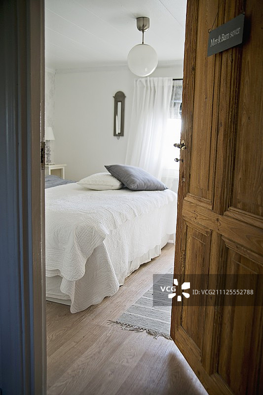 透过开着的门，可以看到质朴的卧室里的白色床罩和散落的靠垫图片素材