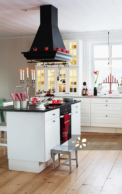 在斯堪的纳维亚乡村别墅厨房中，厨房柜台上方的黑色排气罩和木地板上的白色基础单元图片素材