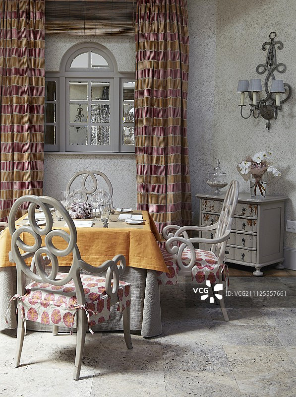 桌子用橙色的桌布和灰色的椅子，椅背上有玫瑰形结构;背景上有条纹及地窗帘的窗户图片素材