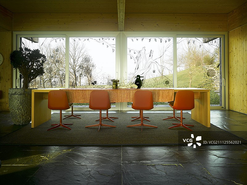 餐厅在木屋与橙色贝壳椅子在长餐桌前玻璃墙与花园的看法图片素材