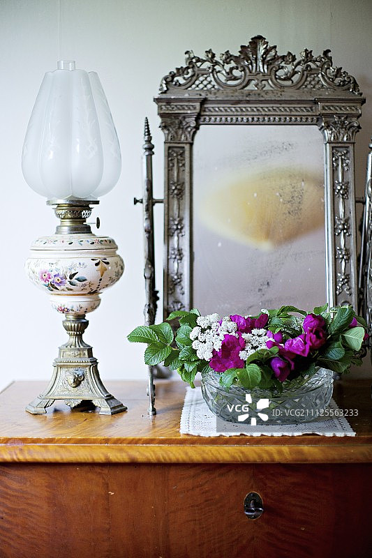 一盏石蜡灯和一碗花，摆在梳妆镜前，简单的木抽屉上有华丽的银框图片素材