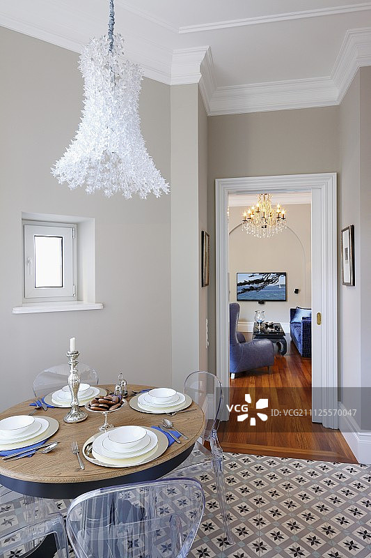 餐厅内装饰有图案瓷砖的地板，装饰有羽毛吊灯的桌椅;透过开着的门可以看到客厅图片素材