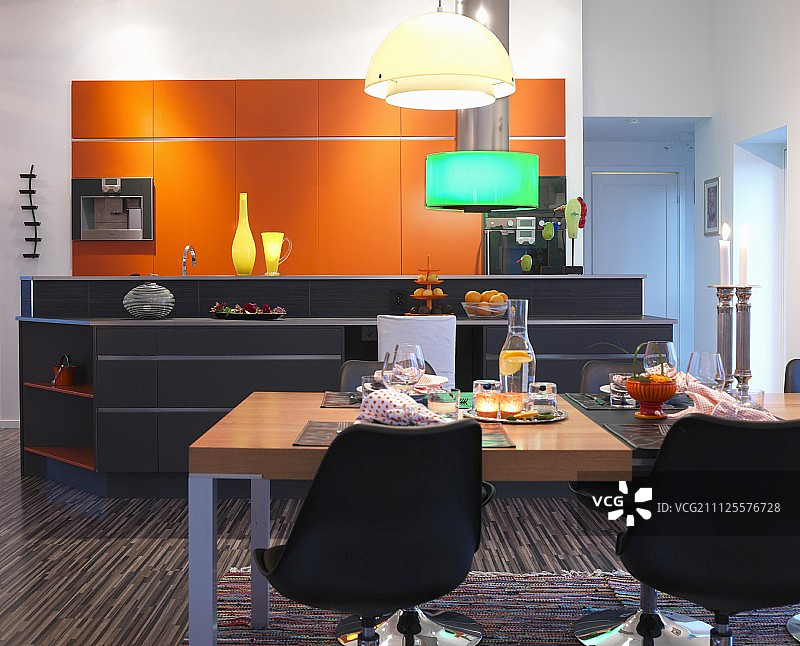 黑色的贝壳椅围绕着餐桌，前面是厨房岛台和橙色的橱柜图片素材