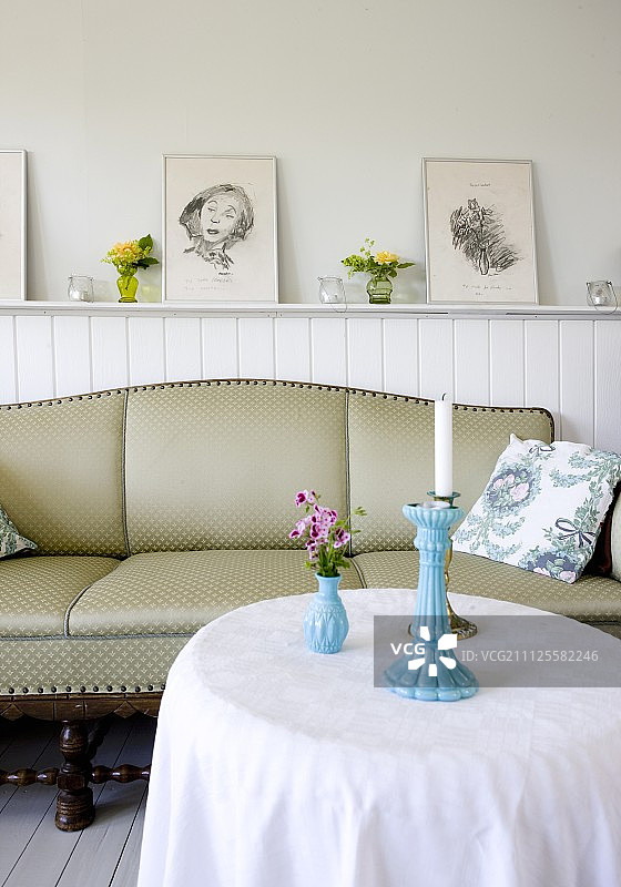 小屋的氛围;圆桌，古色古香的沙发，前面是白色的护墙板，上面有镶框的画图片素材