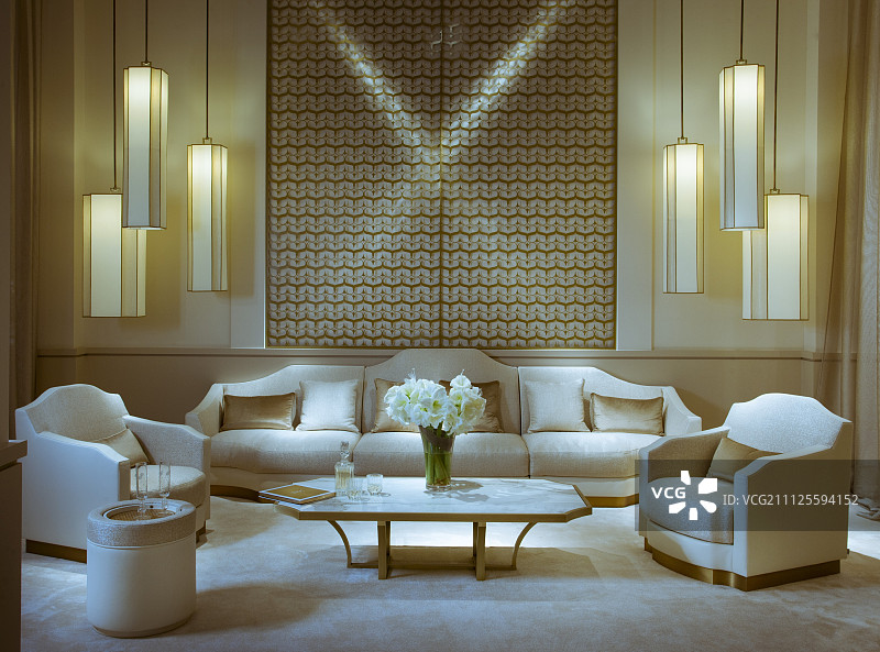 正式布置的扶手椅、沙发套、茶几和一组组吊灯挂在白色和金色的几何墙面前图片素材