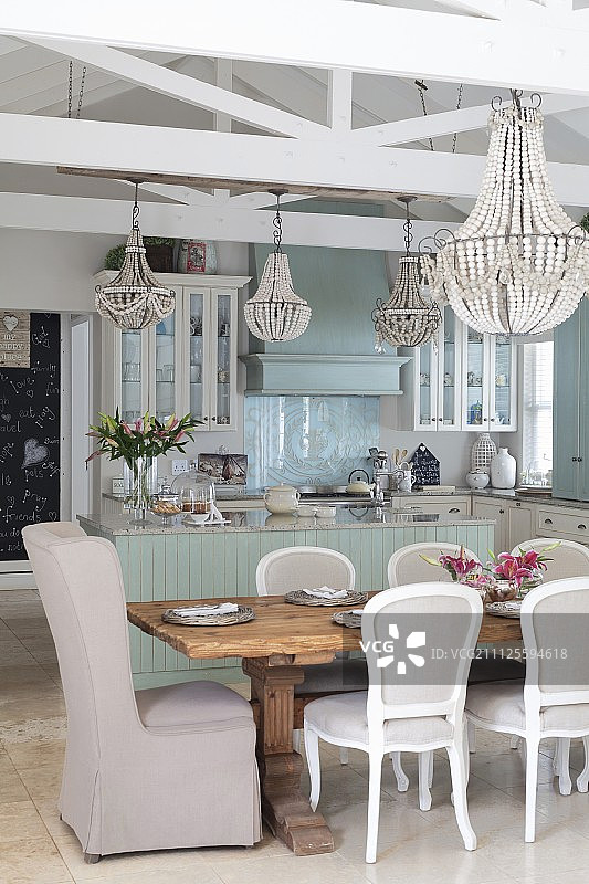 开放式厨房前的实木桌子周围，餐桌上方的吊灯和洛可可风格的椅子图片素材