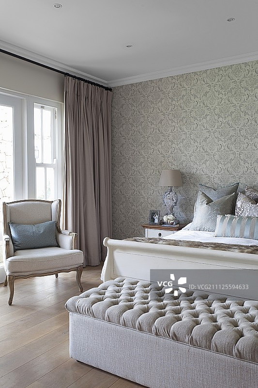 在质朴的卧室里，白色框架的双人床和古董扶手椅的脚凳在窗户前面，有拖地长窗帘图片素材