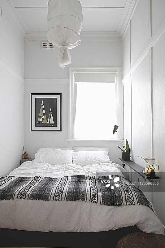 卧室狭窄，窗户下有一张双人床，墙壁和天花板上有简单的白色镶板图片素材