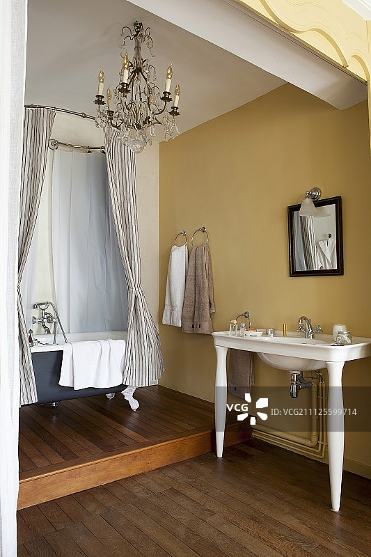 复古风格的浴室，黄色的墙壁，木地板，盥洗台和独立的浴缸在平台上图片素材