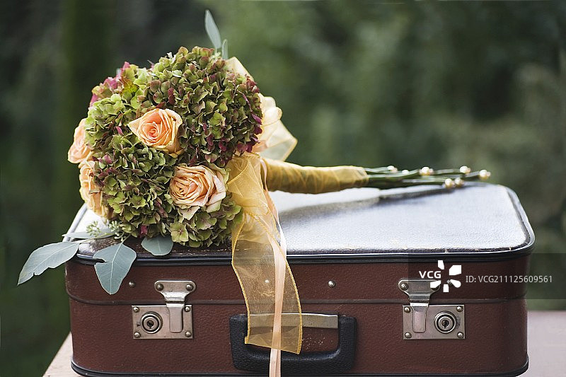 杏花、玫瑰和绣球花的节日花束用丝带系在古董手提箱上图片素材