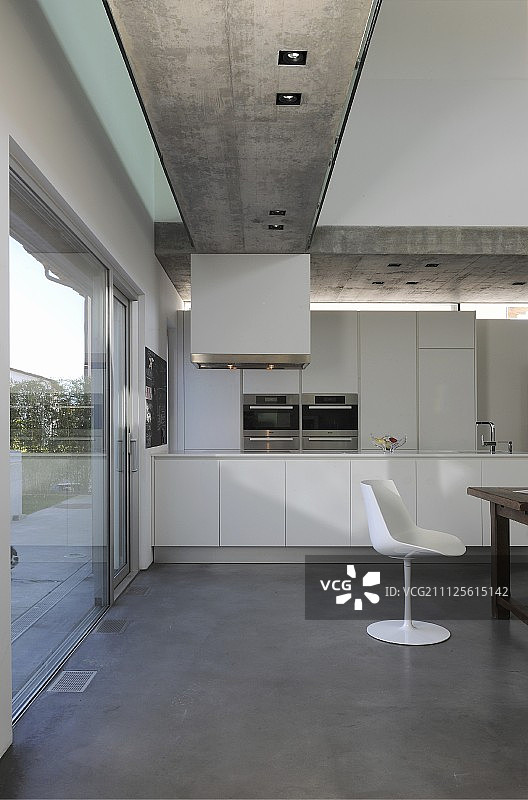 开放式厨房，白色经典贝壳椅和嵌入式射灯在暴露的混凝土天花板在现代住宅图片素材