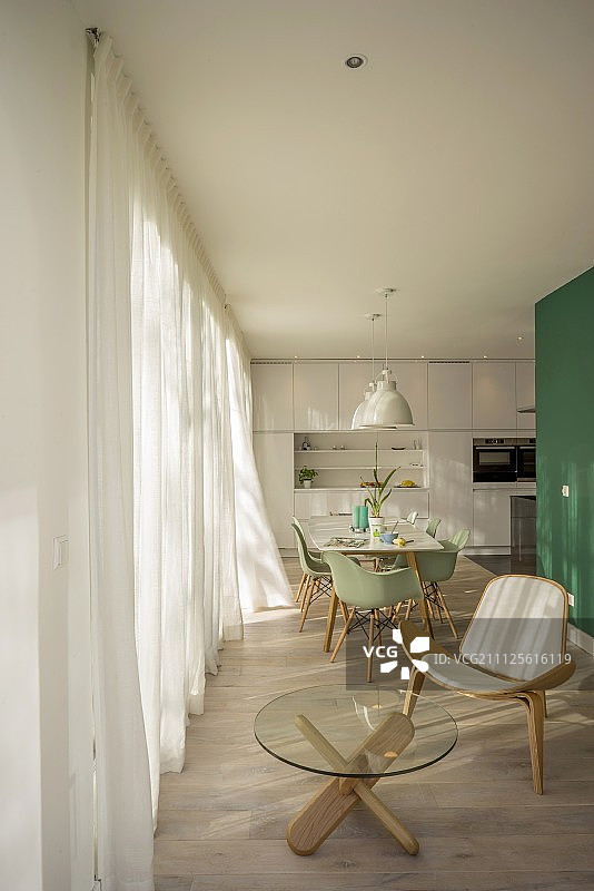休息区的Wegner Shell椅子和玻璃桌子，用餐区的薄荷绿色经典椅子和白色，配备设计师厨房图片素材