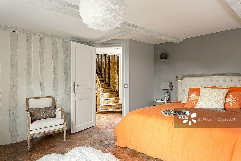 双人床和橙色床单在翻新的卧室与乡村木楼梯的观点图片素材