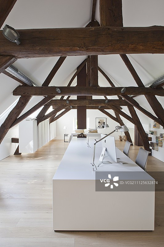经过改造的阁楼里有质朴的屋顶横梁和白色设计师办公桌图片素材