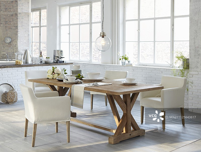 质朴的餐桌和白色软垫椅子，开放式厨房配有工业玻璃图片素材