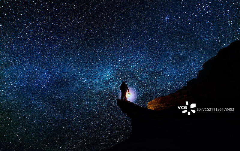 一个人站在悬崖上，身后是星空。图片素材