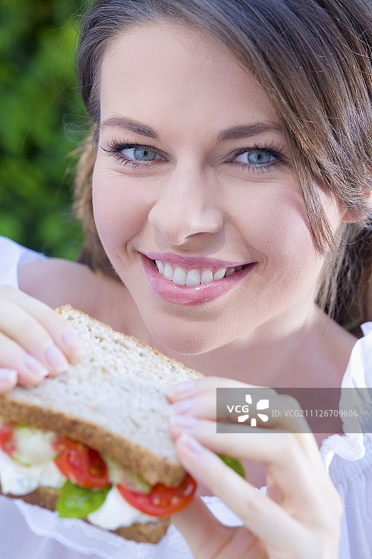 年轻女子吃着白干酪、番茄和罗勒三明治图片素材