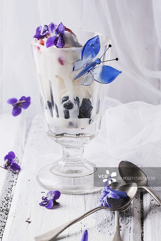 一个冰淇淋圣代，里面有香草冰淇淋、水果果冻和蓝莓，并用糖紫罗兰装饰图片素材