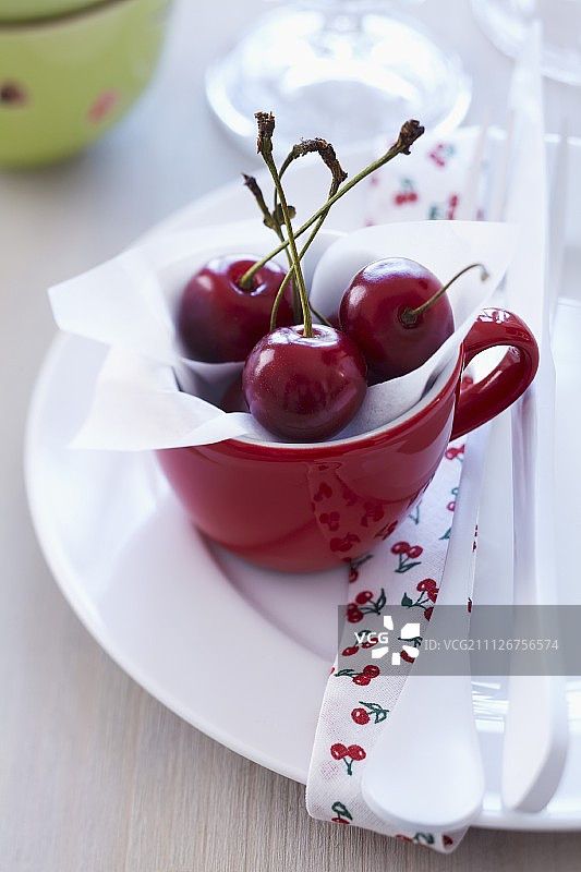 鲜嫩的樱桃装在红杯子里放在盘子里图片素材